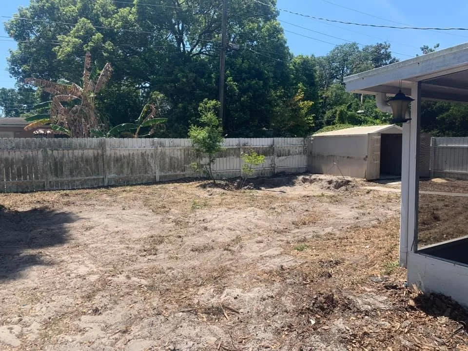 Backyard cleared and graded down to bare sand after a structure removal, with a fence and shed behind