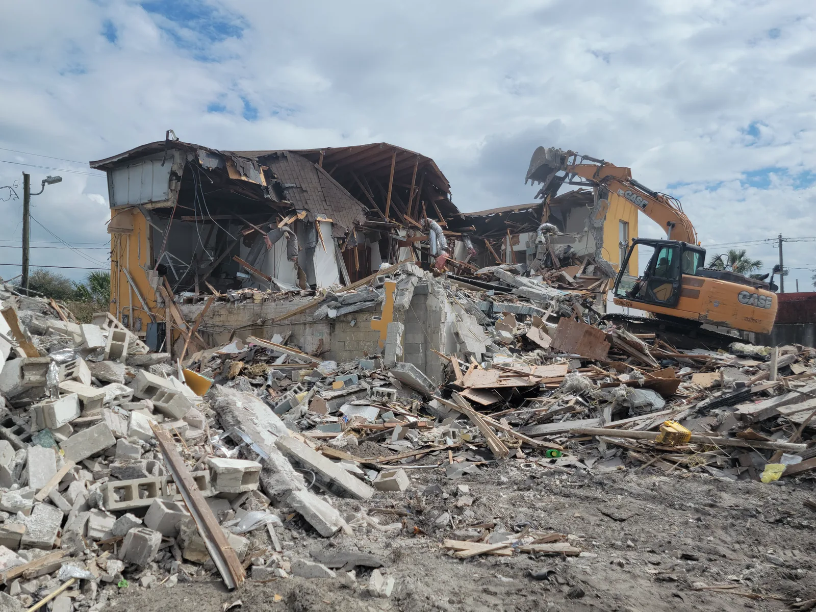 Excavator pulling down the block walls of a large commercial building, with a deep pile of block and lumber rubble in front