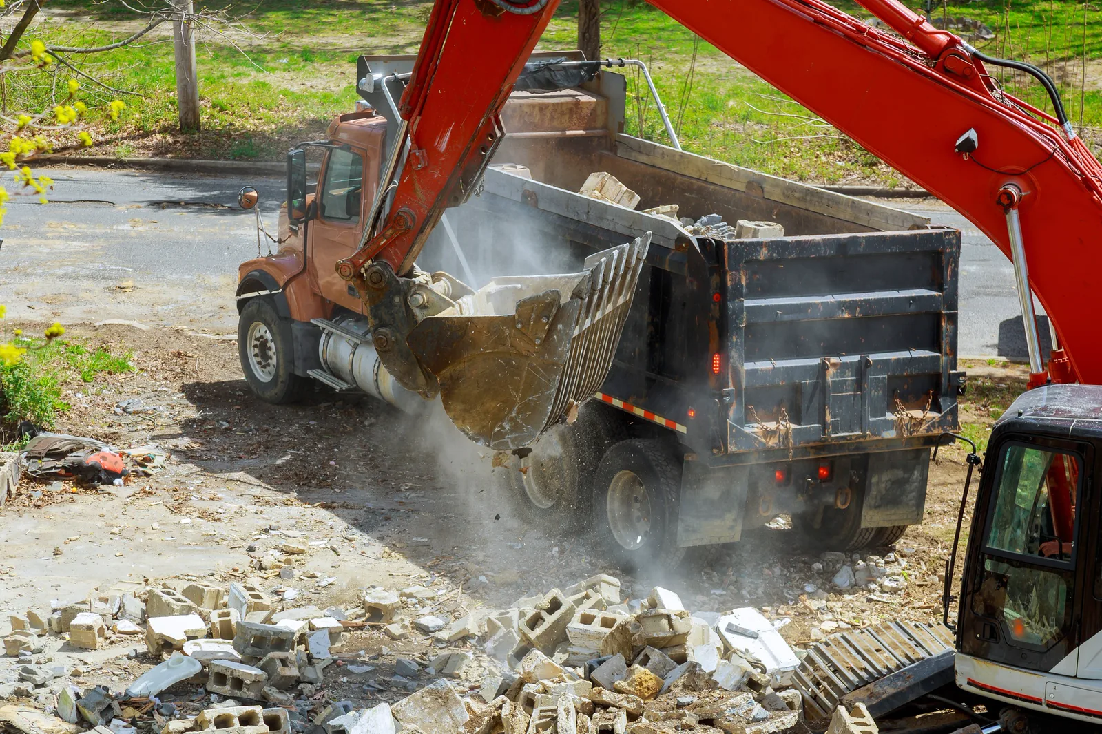 Excavator loading broken concrete block and demolition debris into a dump truck