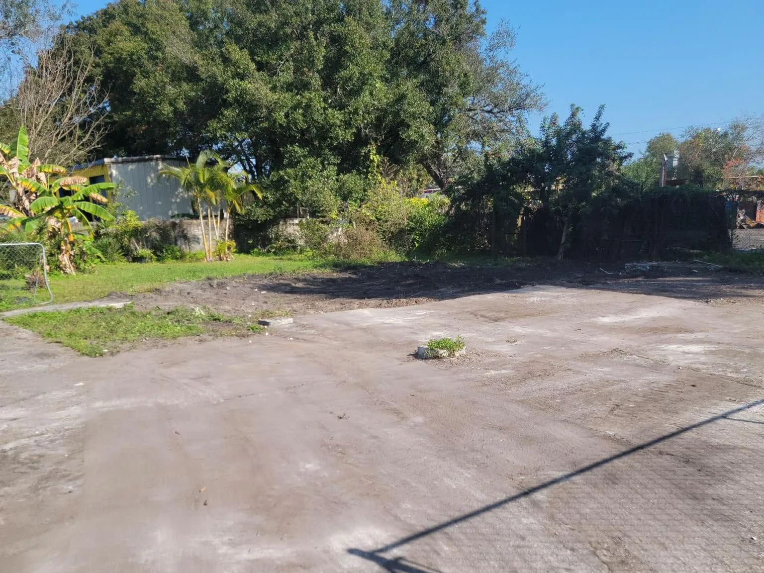 Graded lot after demolition showing the old slab area, a chain-link fence and oak trees along the back