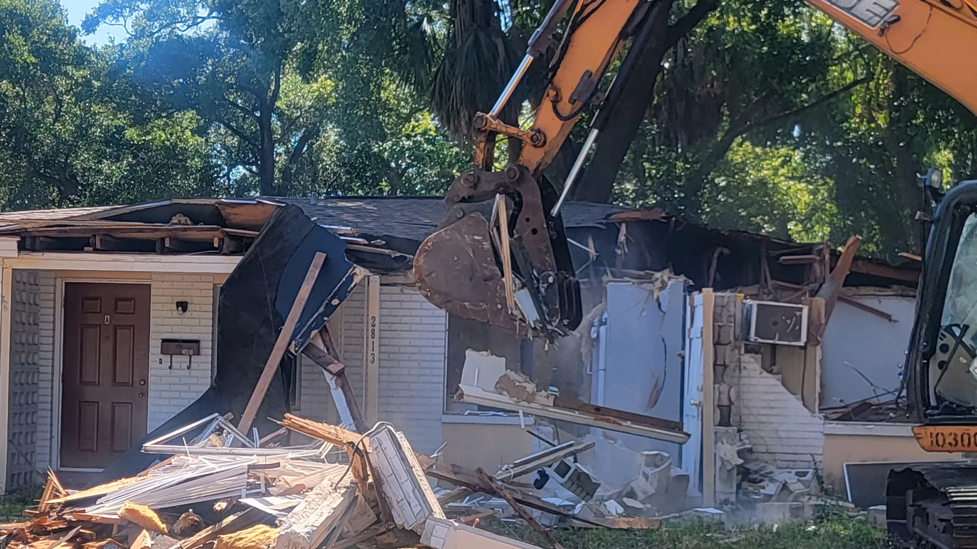 Excavator tearing through the roof of a single-story house during demolition