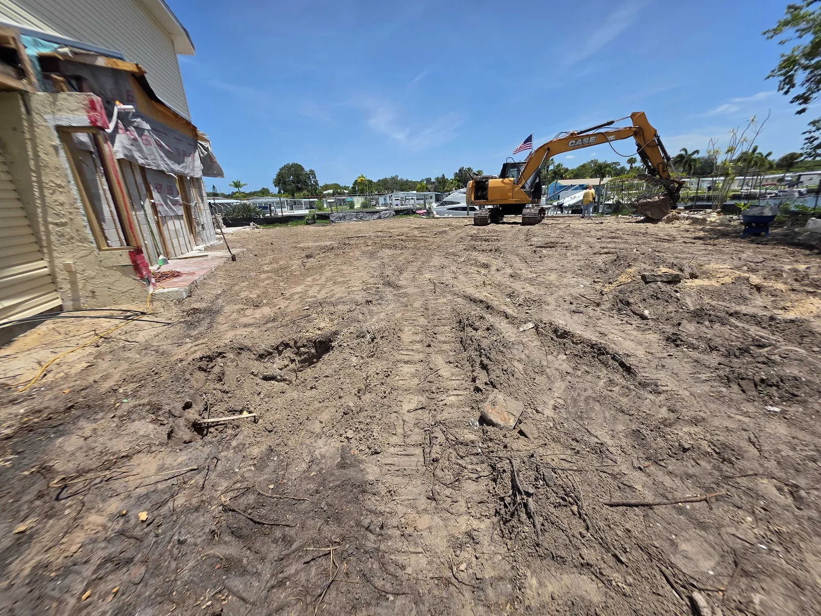Lot cleared to bare dirt after a teardown in the Tampa Bay area, with an excavator loading the last debris at the far end