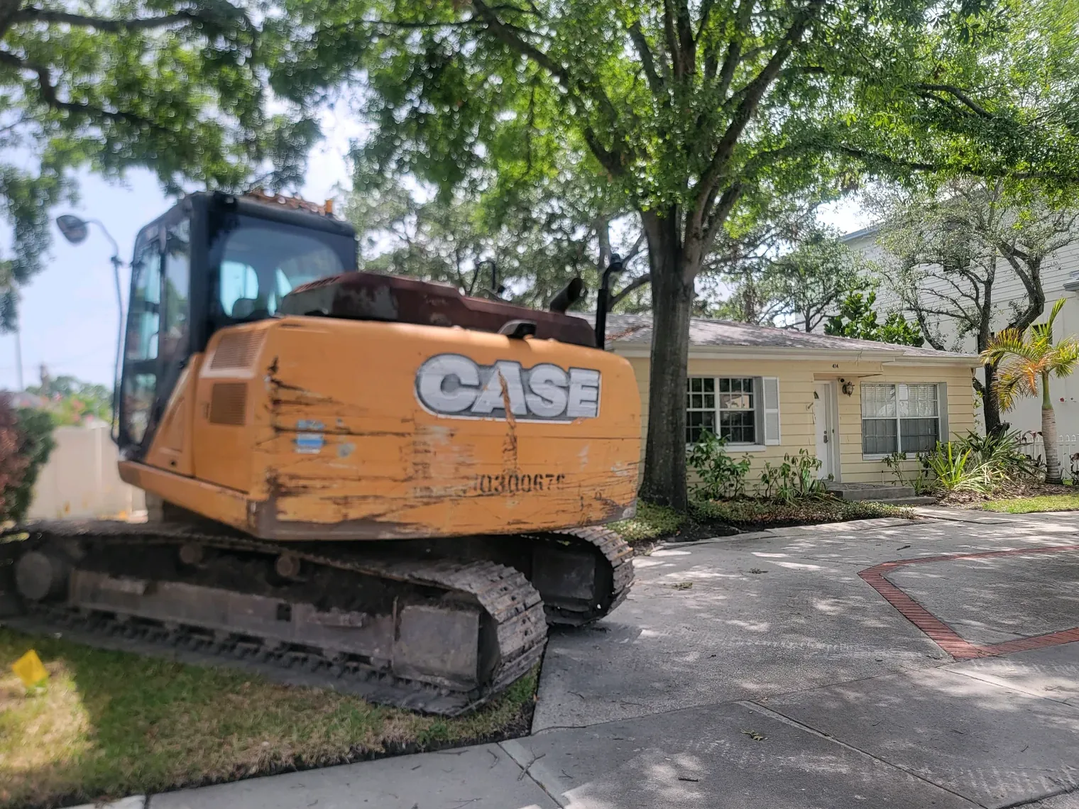 Tracked excavator staged on the driveway of a small yellow house before a house demolition in the Tampa Bay area