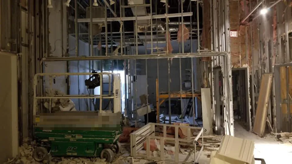 Commercial interior stripped to the metal studs with the ceiling grid removed and a scissor lift parked in the gutted space