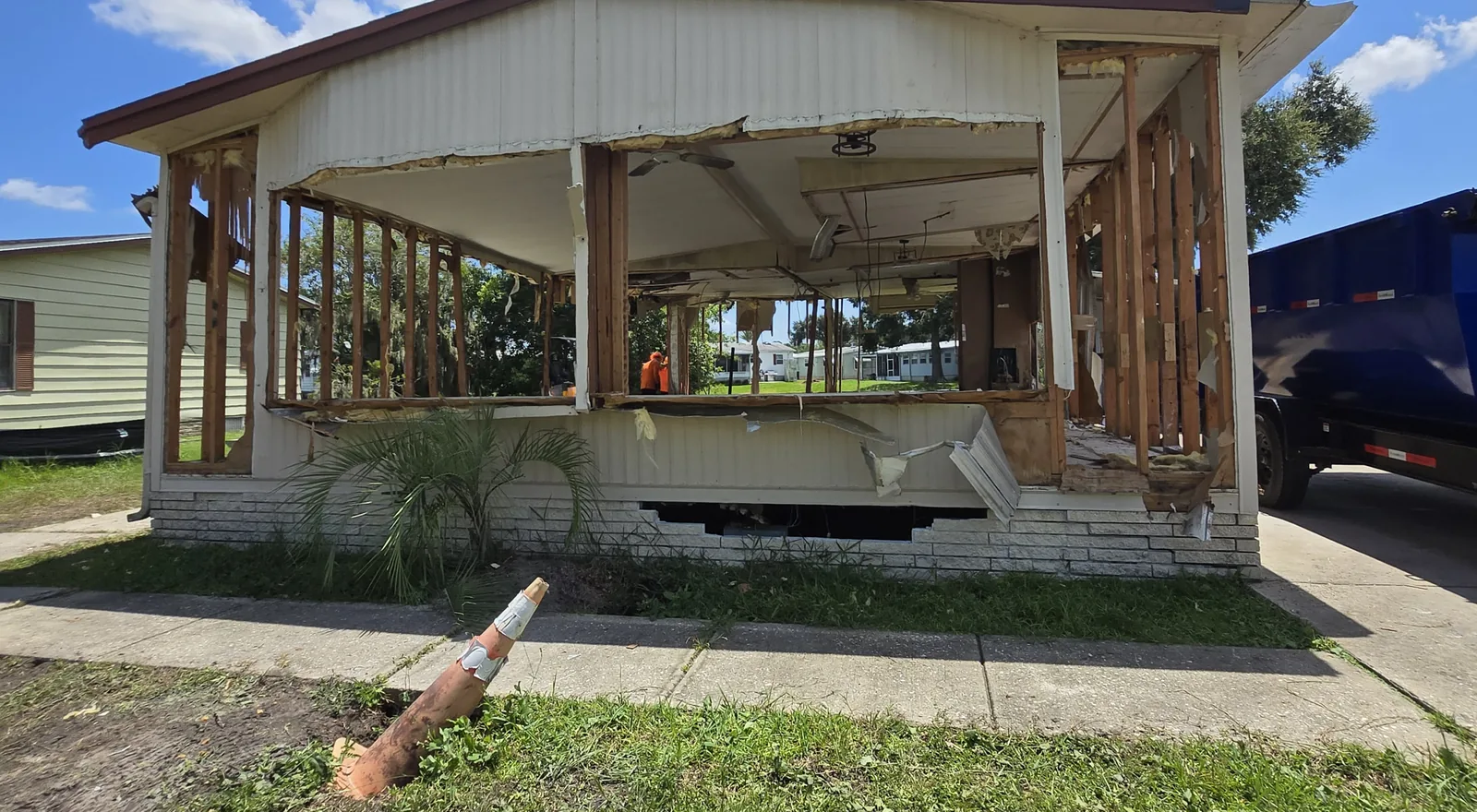 Mobile home stripped down to its framing during removal, with an unmarked dump trailer backed up alongside
