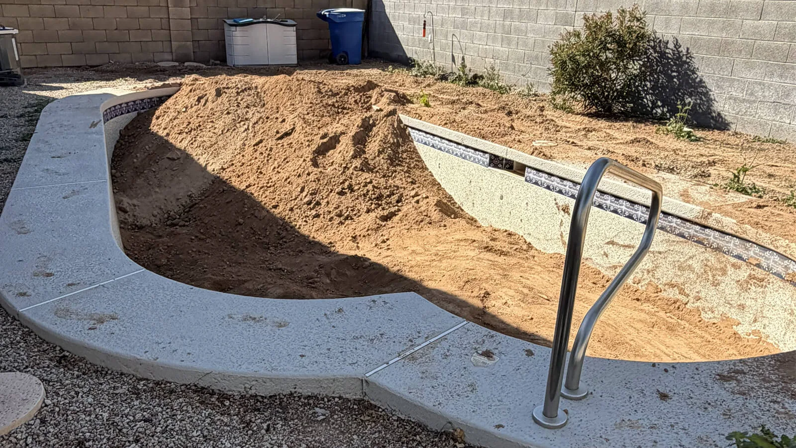 Inground pool shell being filled with dirt, with the coping and handrail still in place