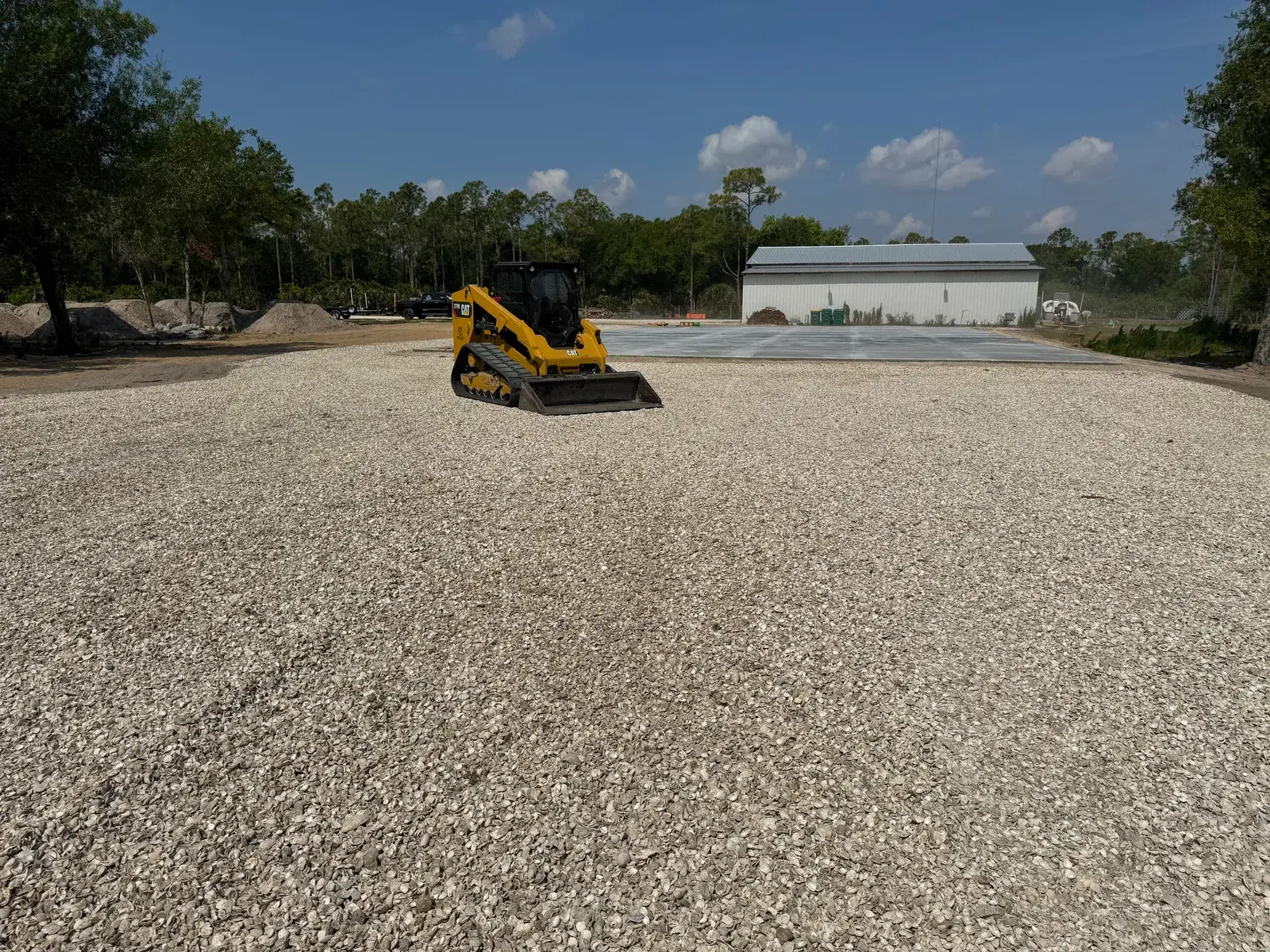 Compact track loader on a compacted limerock building pad next to a finished concrete slab during site prep