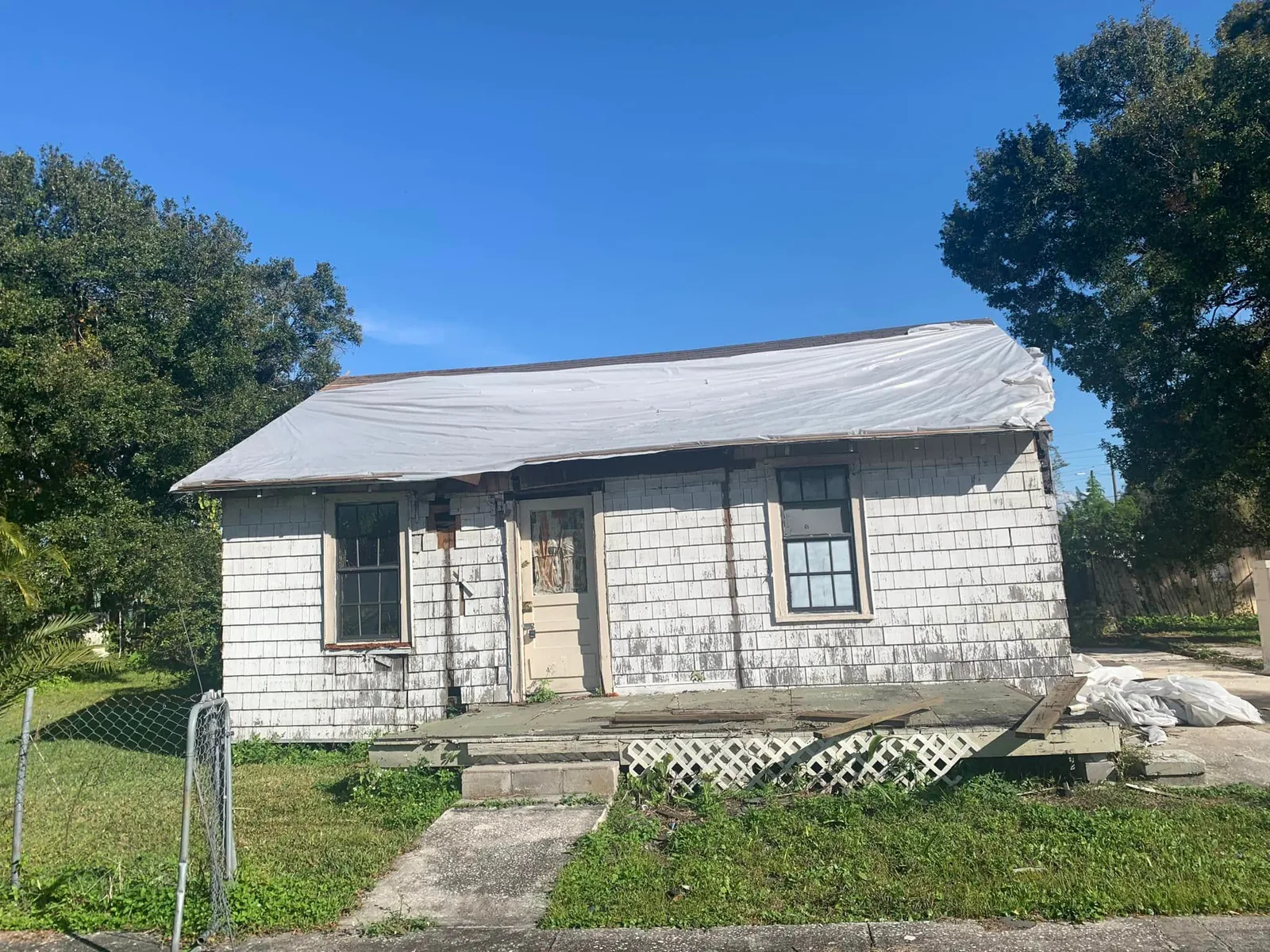 Old white wood-sided house with a blue-tarped roof, waiting to be demolished