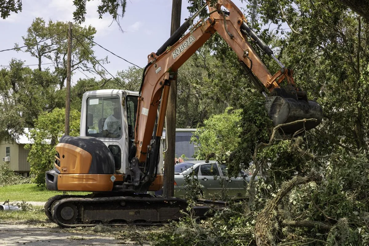 Compact excavator clearing downed tree limbs and storm debris from a residential yard